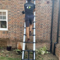 Home Window cleaner in branded uniform climbing a ladder to access high-level windows in Enfield Town.