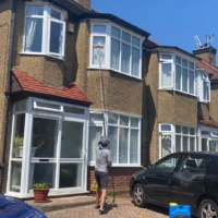 Home Professional window cleaner using a water-fed pole to clean bay windows of a semi-detached house in Enfield.